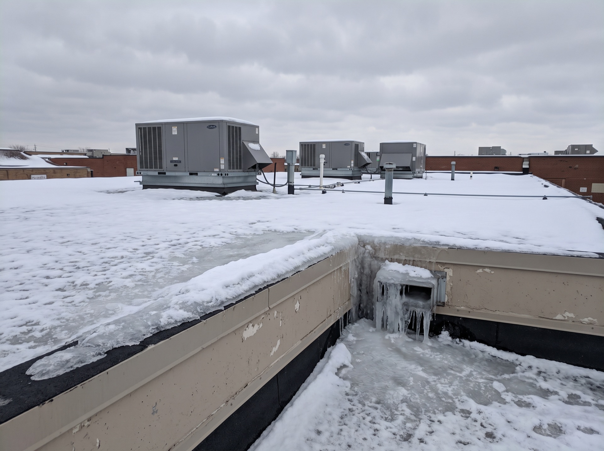 Frozen roof drain at commercial flat roof parapet wall covered in snow and ice