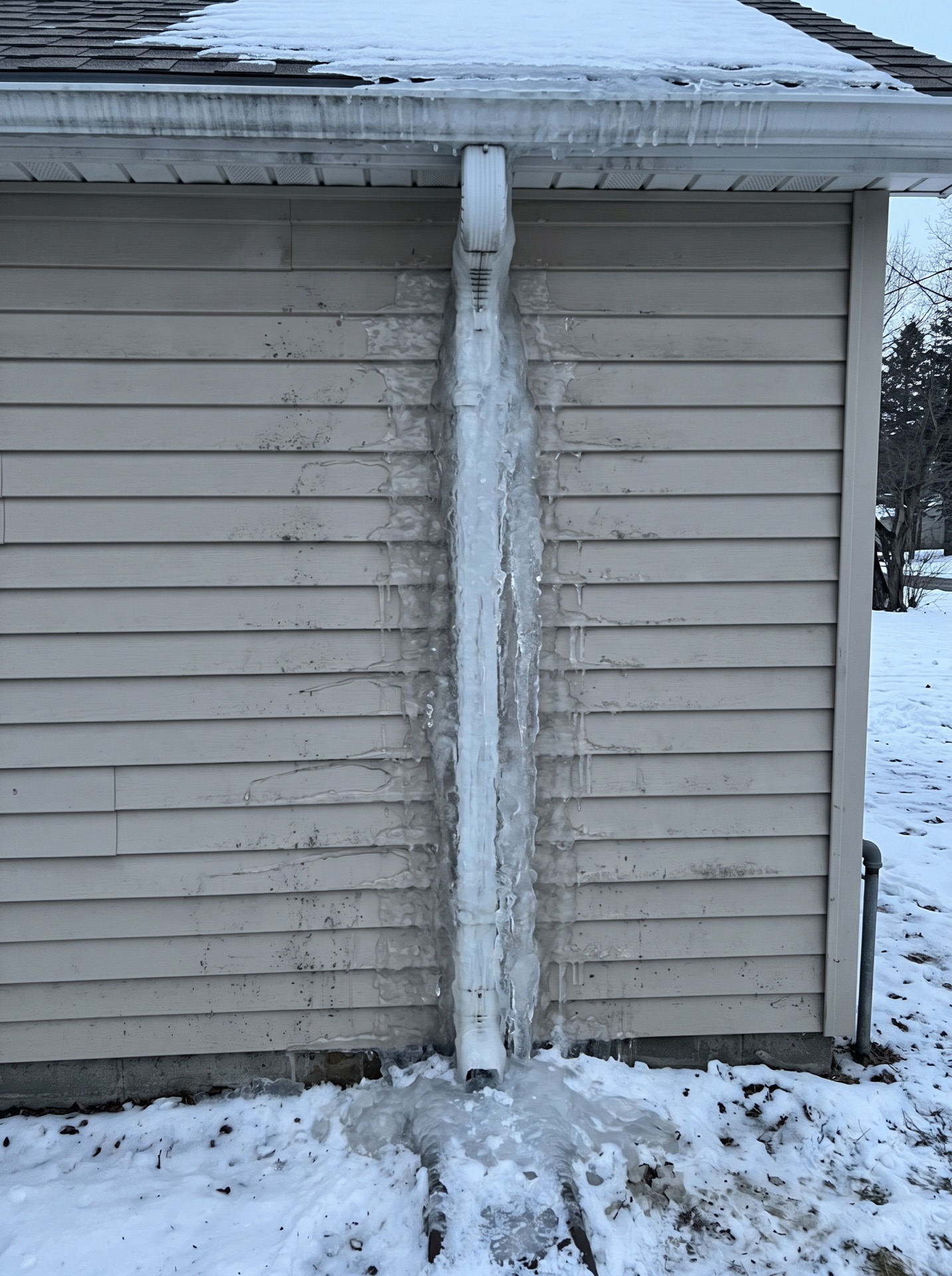 Frozen downspout encased in thick ice column against white vinyl siding