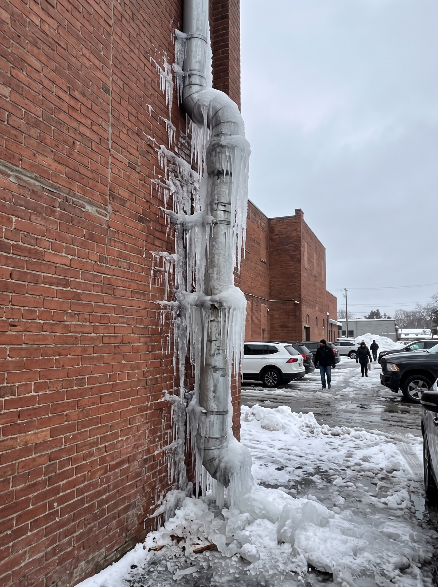 Frozen downspout covered in large icicles on brick commercial building in winter