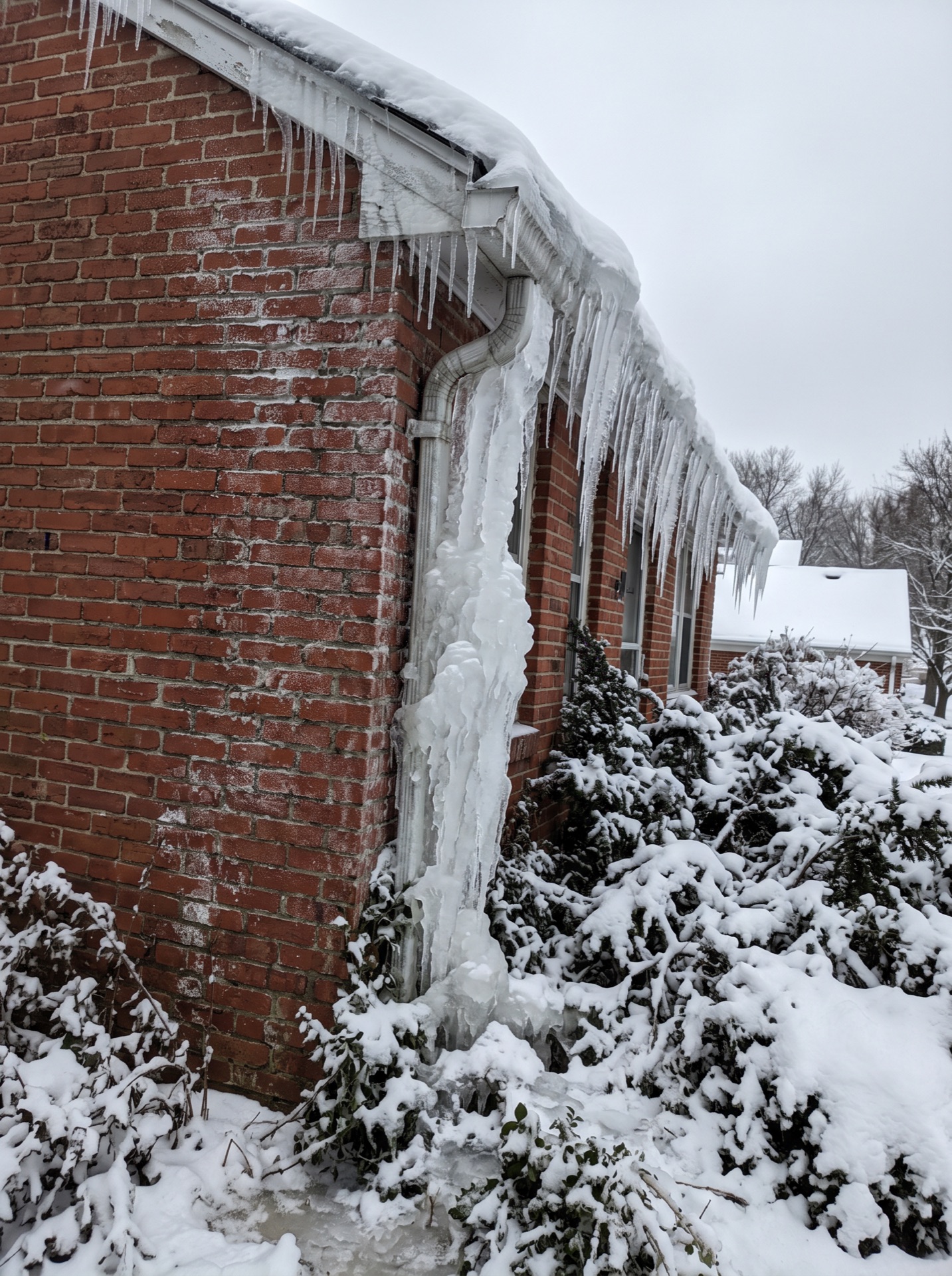 Frozen downspout and large icicles covering brick house exterior in winter