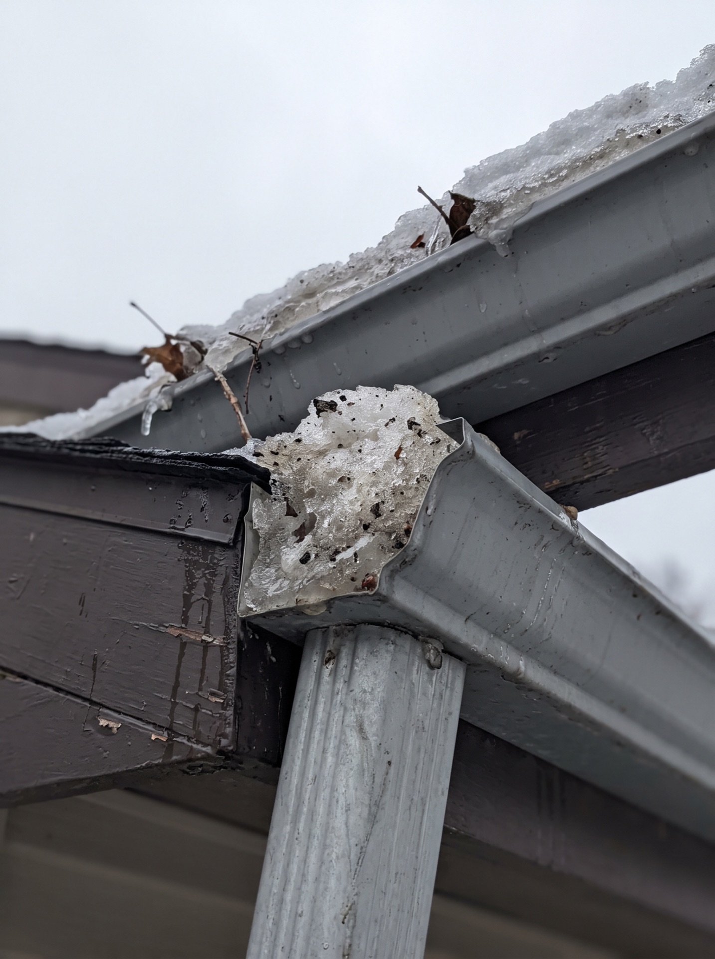gutter outlet and downspout corner packed with ice and debris in winter