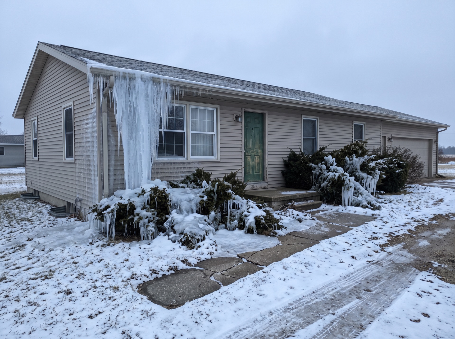 Massive icicles and ice sheets frozen down the front wall of a ranch house