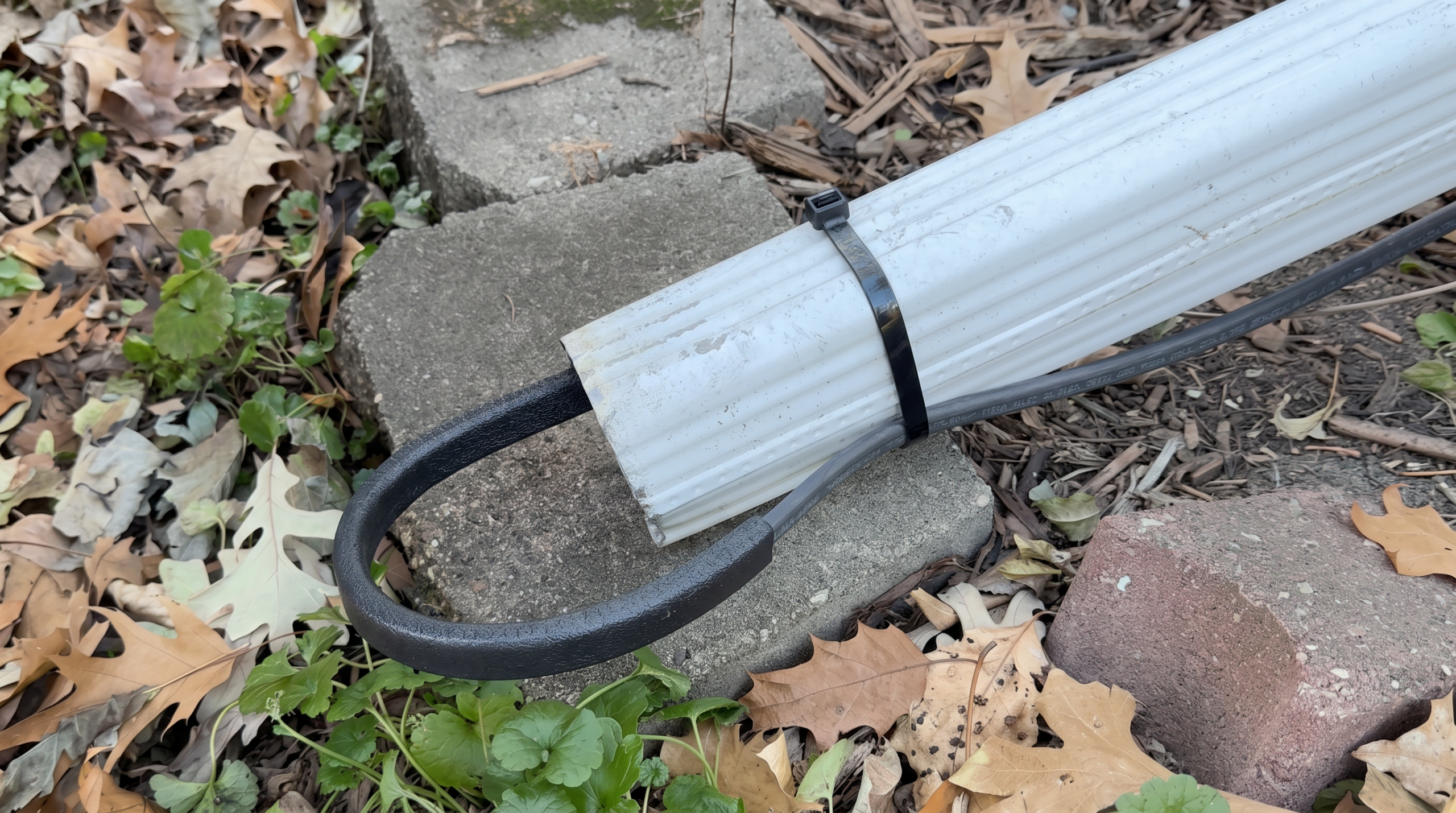 Heated downspout cable secured with black zip tie on white corrugated drain pipe