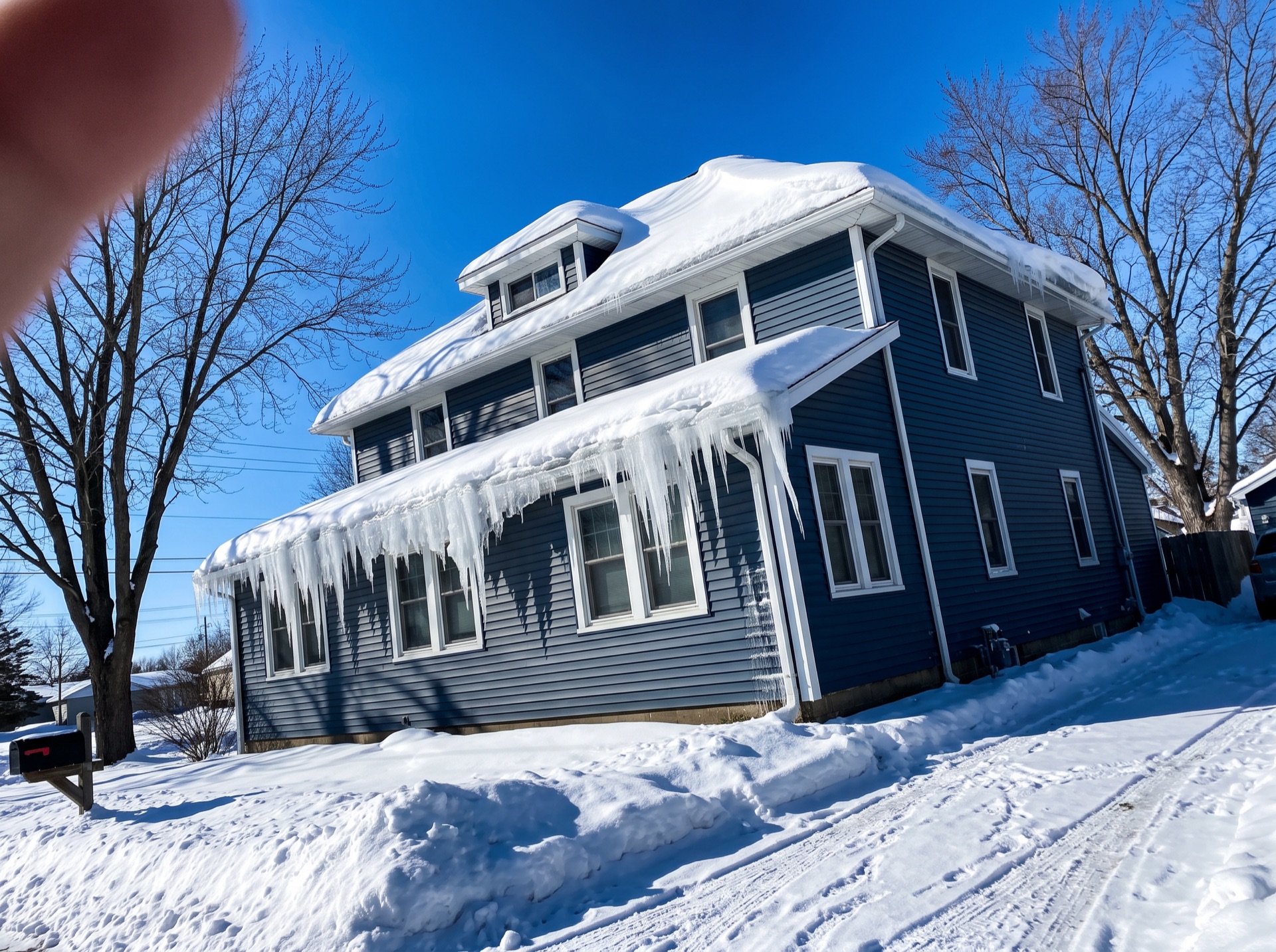 Blue two-story house with heavy snow load and large icicles on roof edge