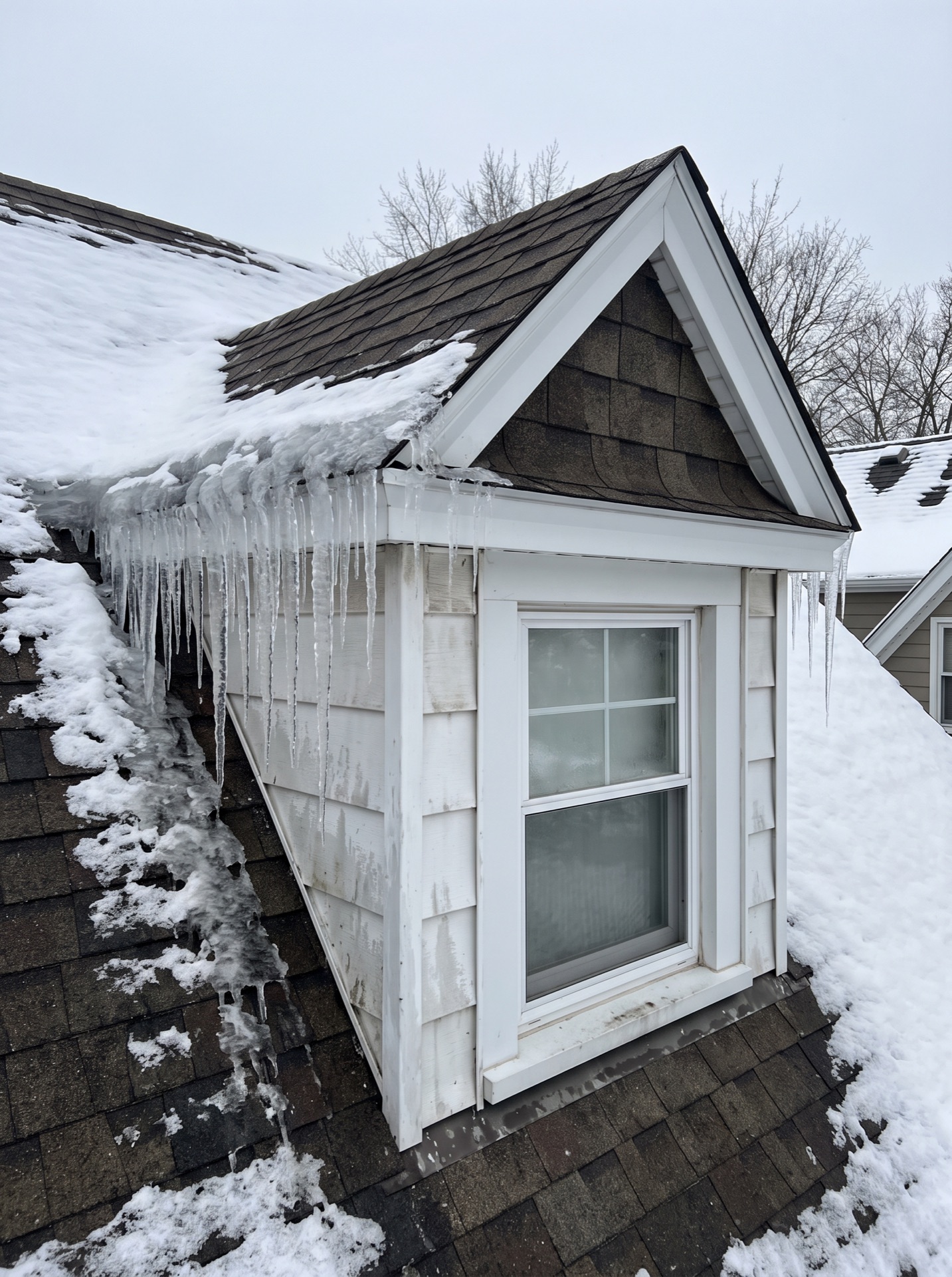Ice dam with large icicles forming along dormer window roof edge