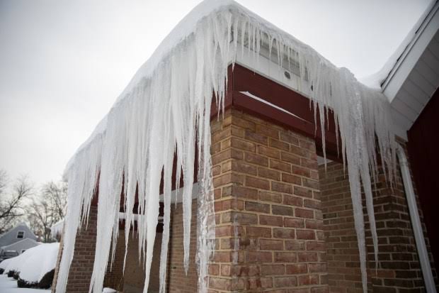 Large icicles and ice dam buildup along the edge of a brick home roof