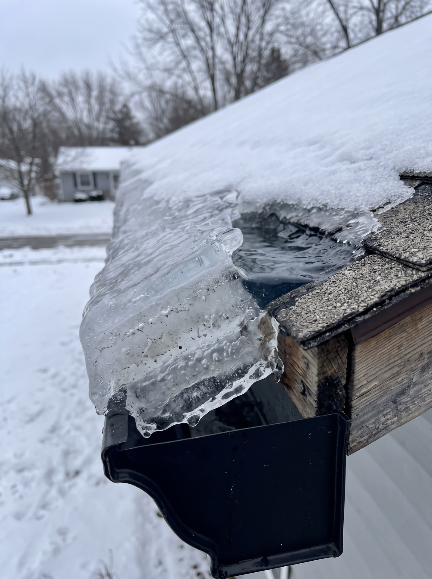 Ice dam cross-section on roof gutter with trapped meltwater pooling underneath snow