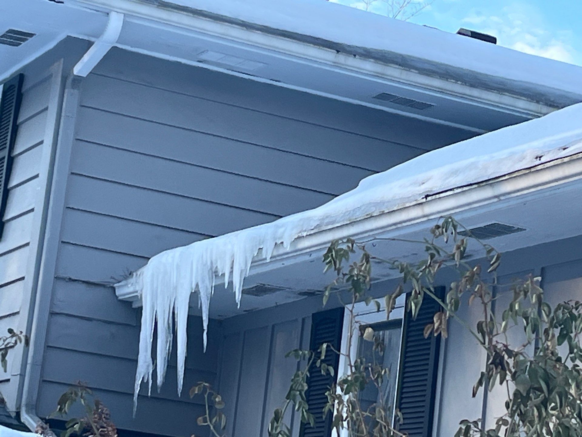 Large icicles and ice dam forming along gutters of gray house in winter