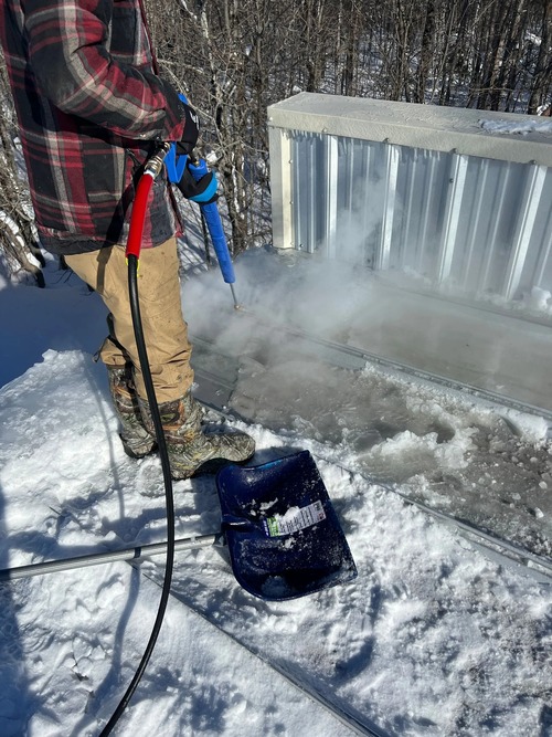 contractor using steam equipment to remove ice dam from snowy roof