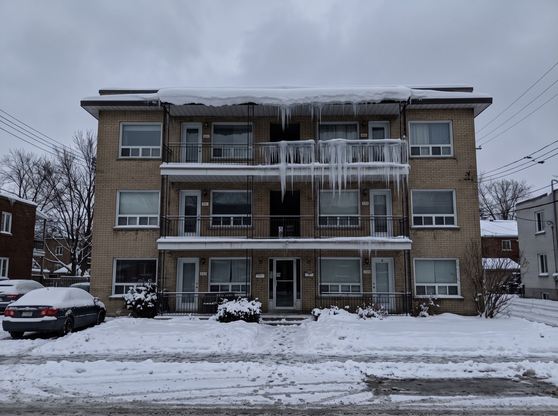 Large ice dam with icicles hanging from apartment building roof eave in winter