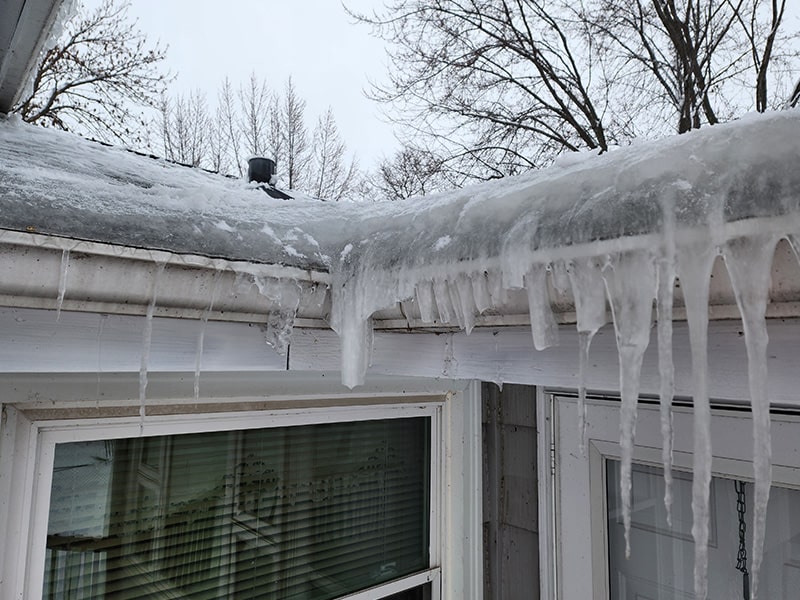 Large ice dam with hanging icicles along residential roof edge and gutters