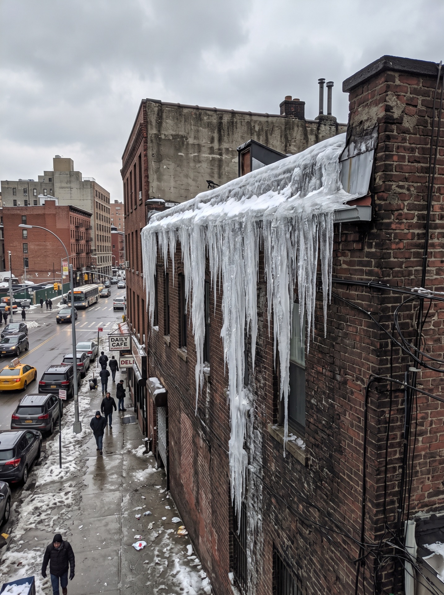 Large icicles hanging from snowy rooftop of brick building on urban New York City street