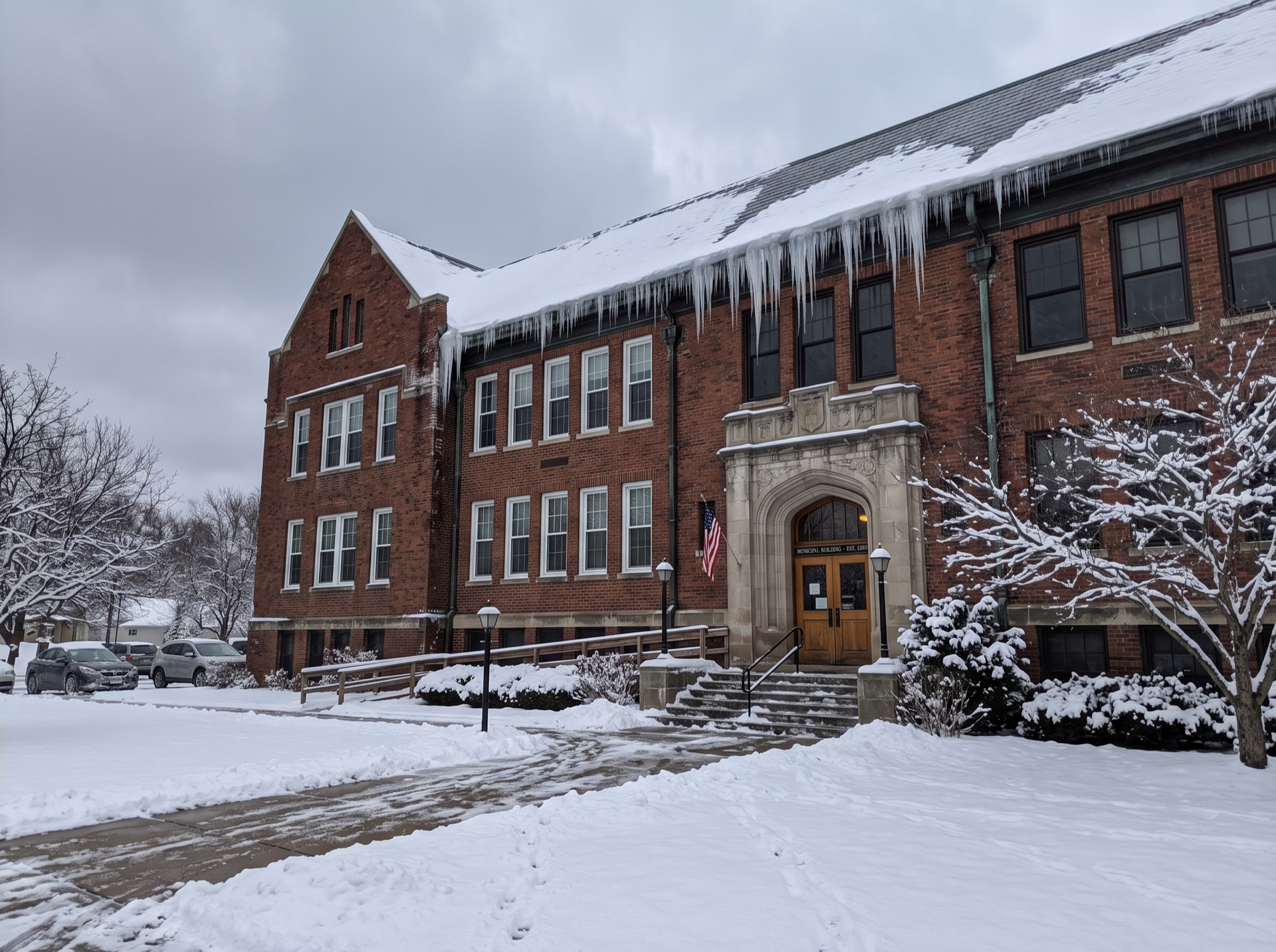 Large icicles hanging from brick municipal building roofline covered in snow
