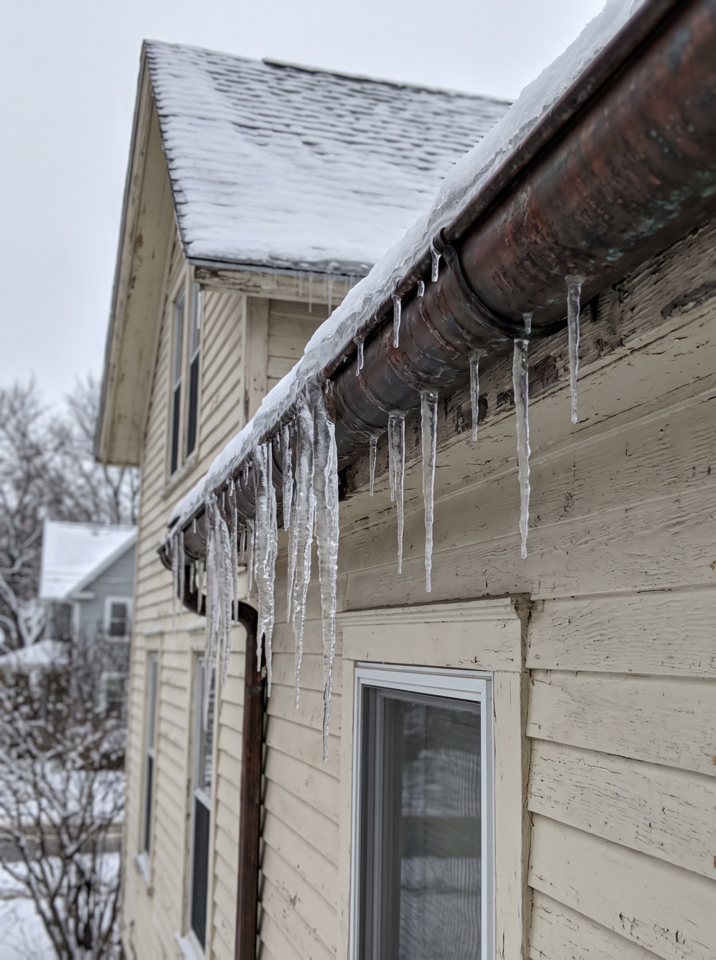 Icicles hanging from a rusty copper gutter on an old two-story house in winter
