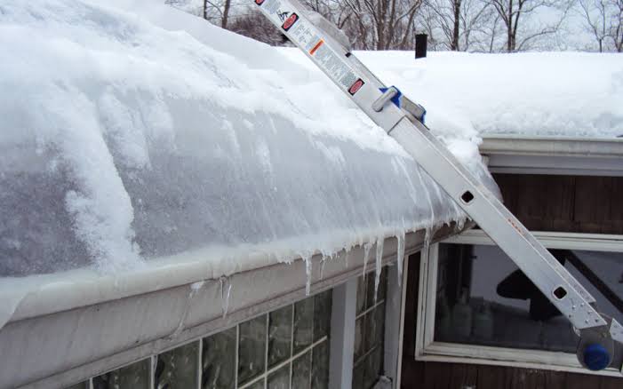 Aluminum ladder leaning against snow-covered roof with icicles and ice dam on gutter