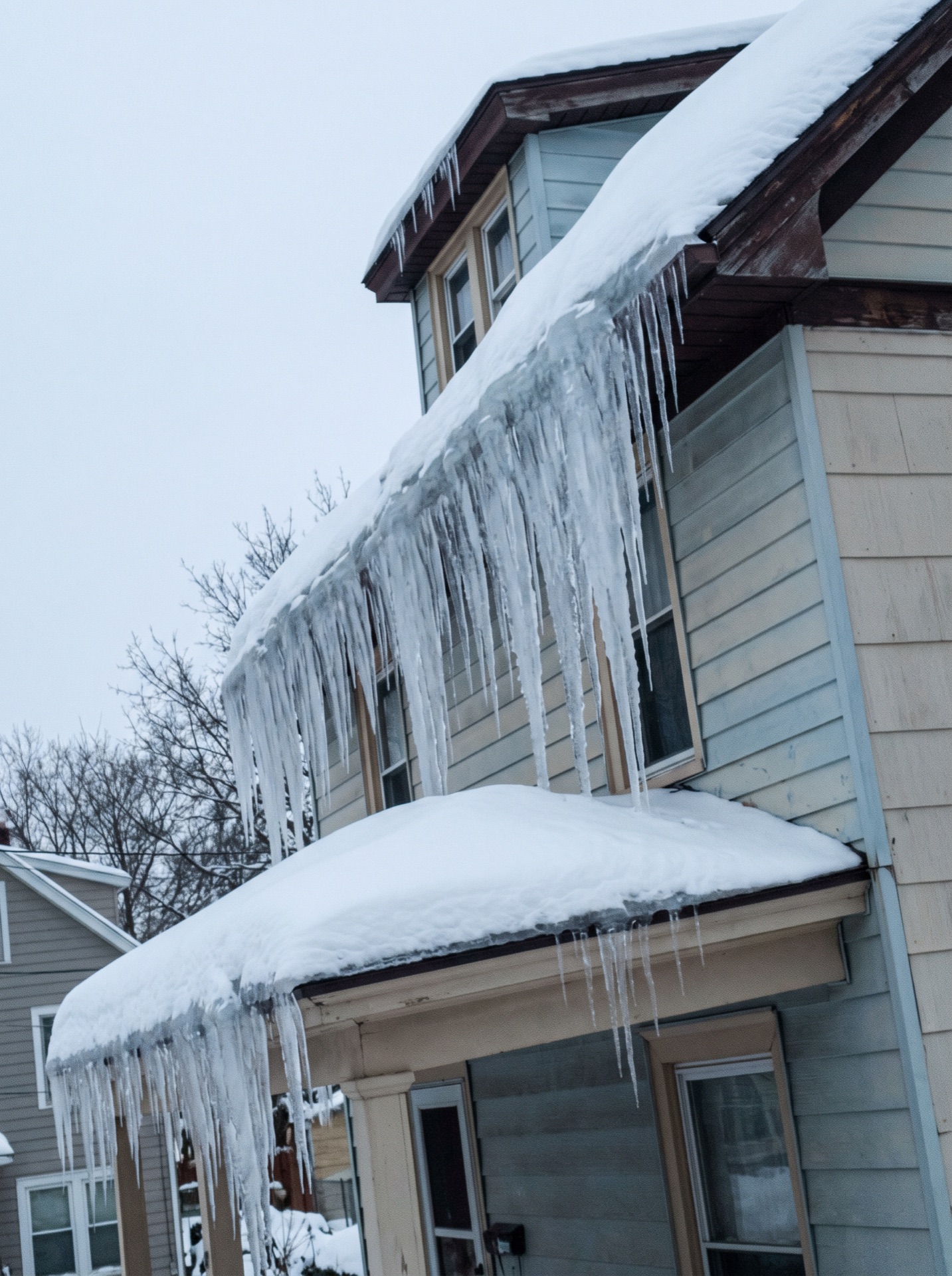 Large icicles hanging from second-story eave down to snow-covered porch roof