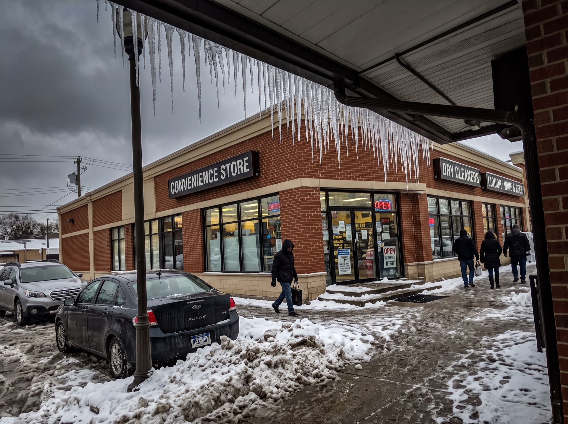 Large icicles hanging from strip mall canopy over snowy parking lot in winter