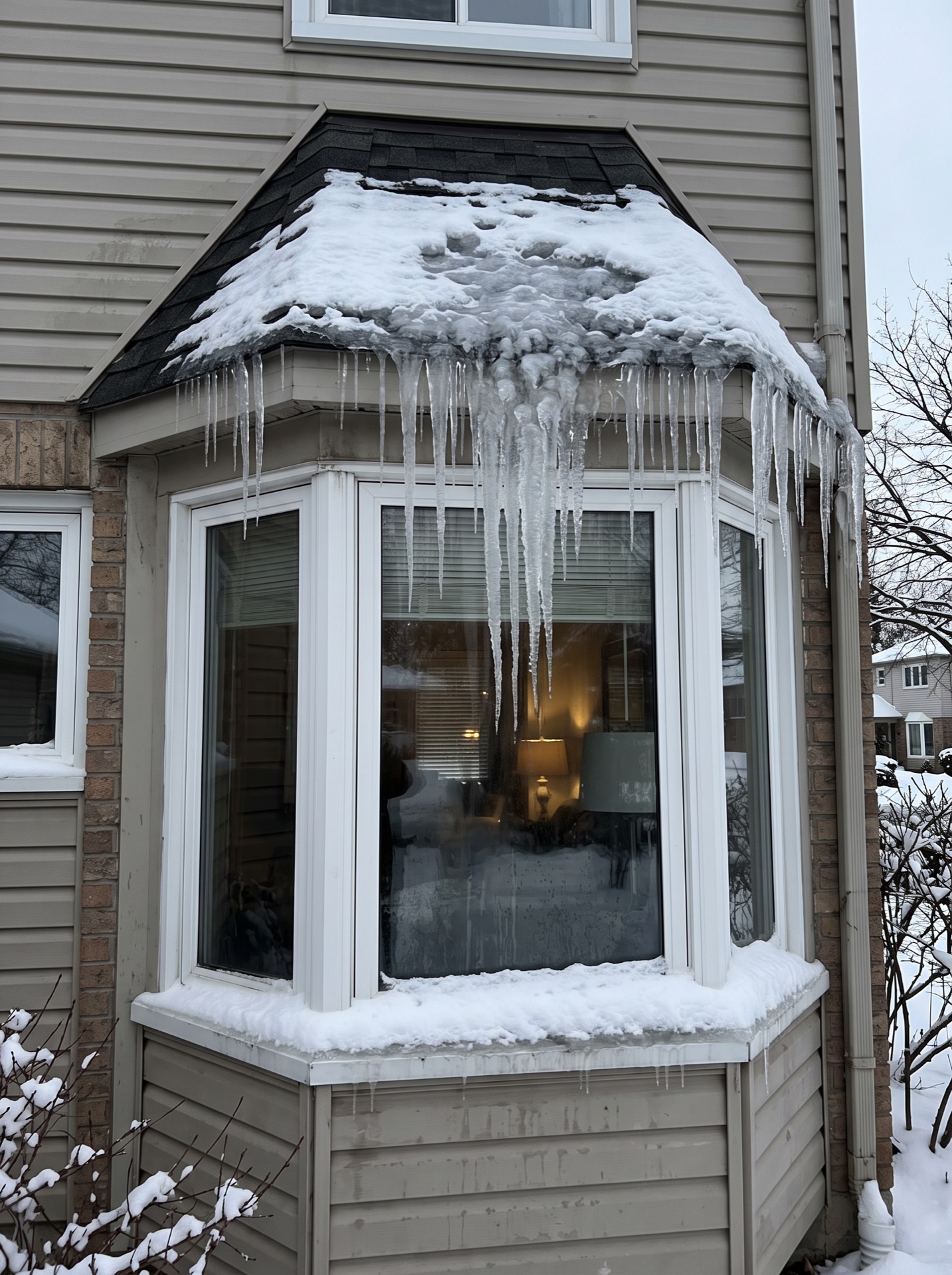 Large icicles hanging from snow-covered bay window roof in winter