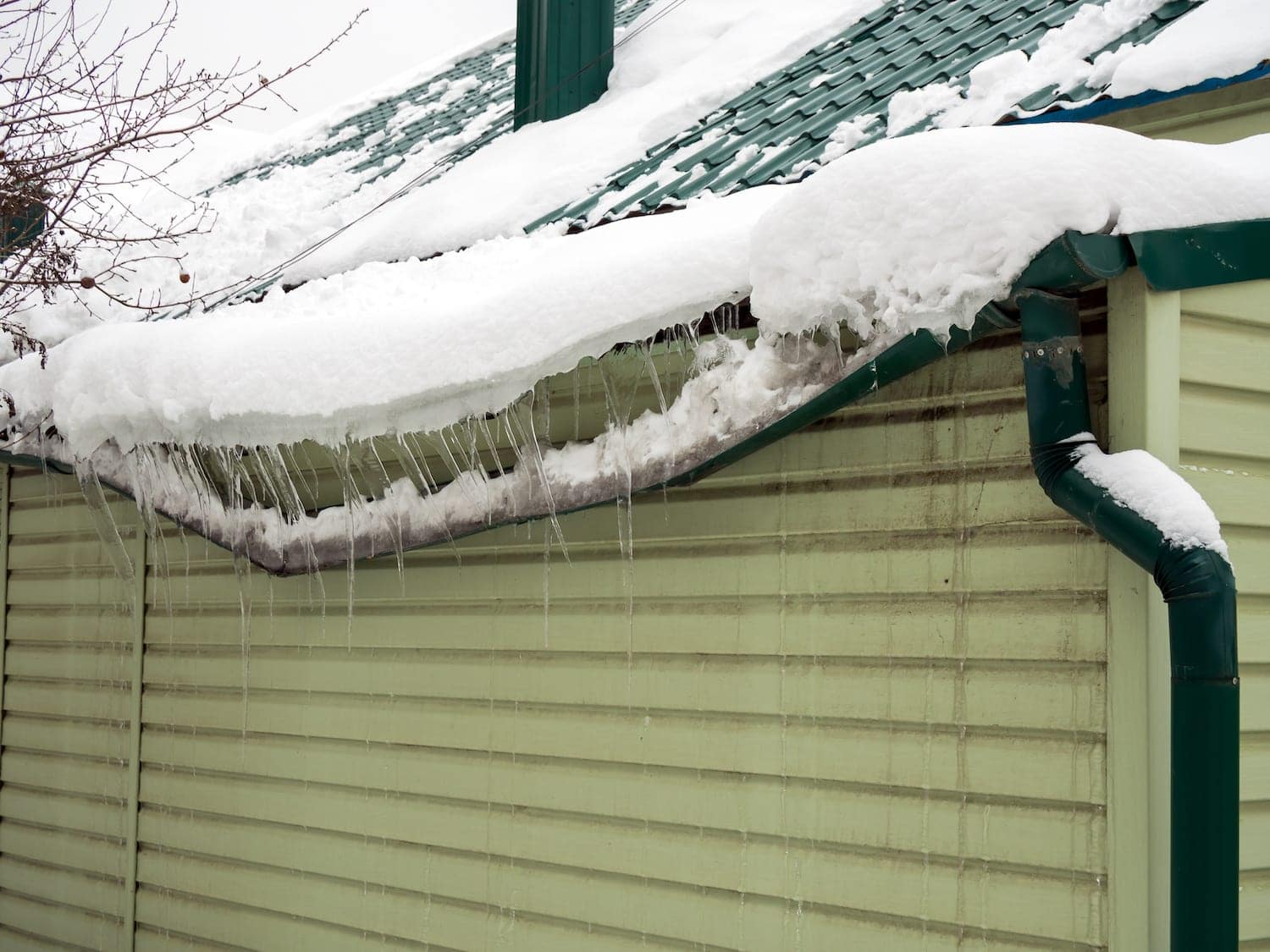 Heavy snow and ice dam pulling green rain gutter away from roof edge