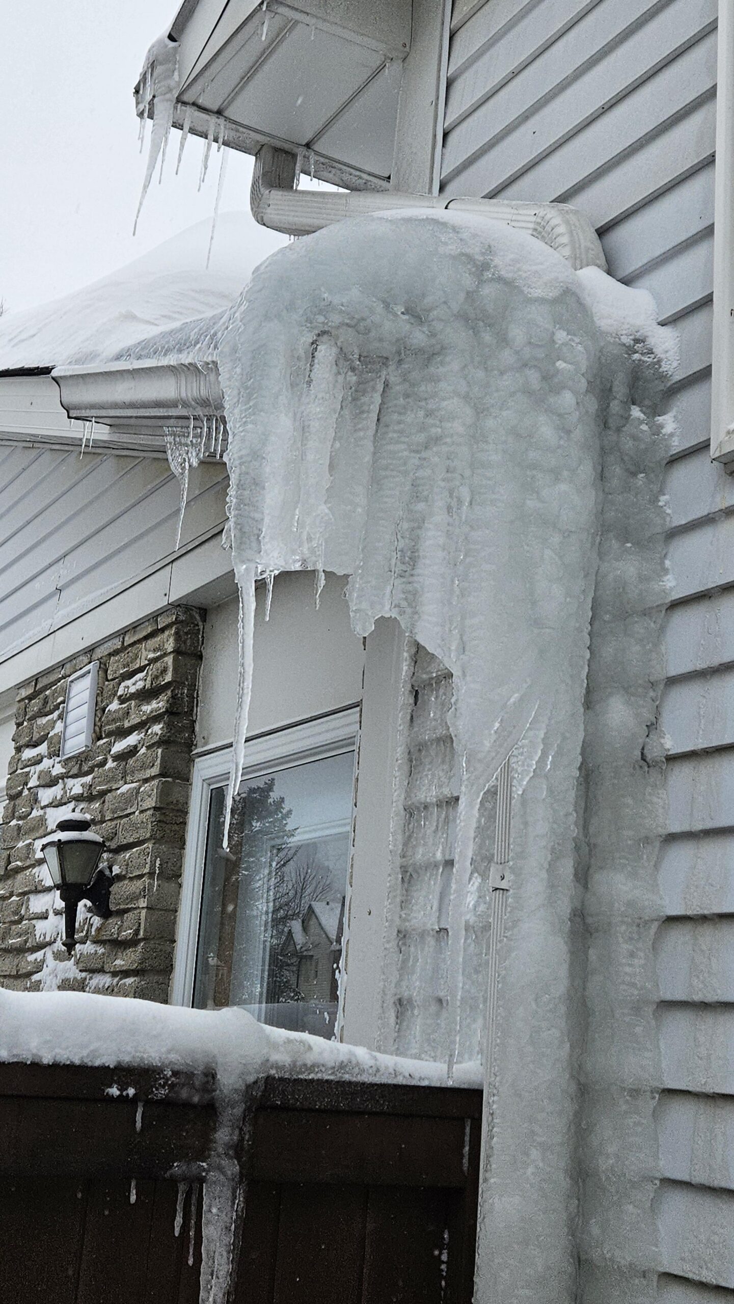 Massive ice dam and icicles encasing a residential downspout and roof edge