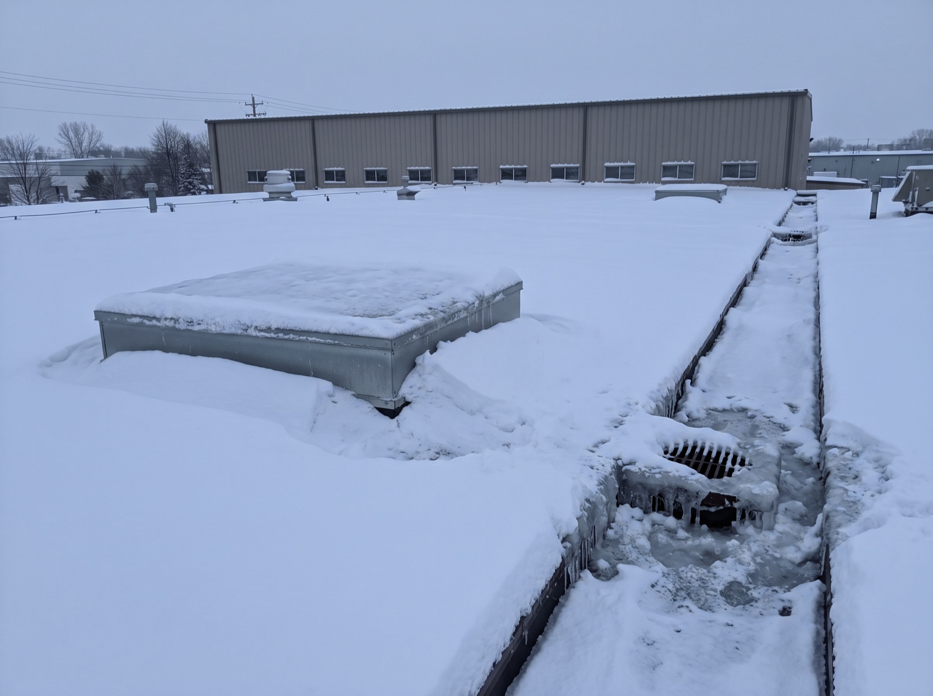 Heavy snow load on flat commercial warehouse roof with frozen drain and icicles