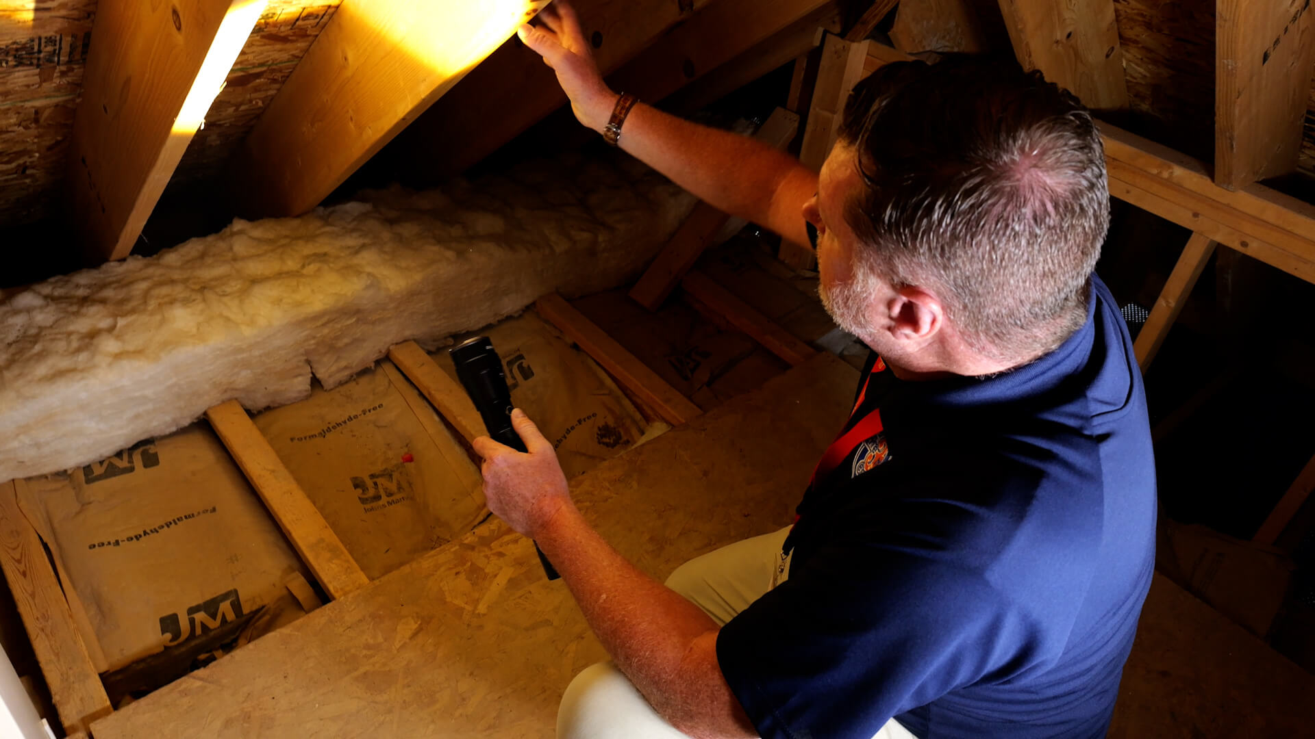 Home inspector using flashlight to examine attic insulation and roof structure