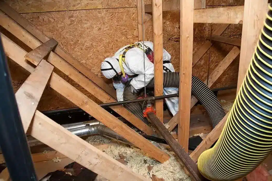 Technician in hazmat suit performing attic mold remediation with vacuum hose