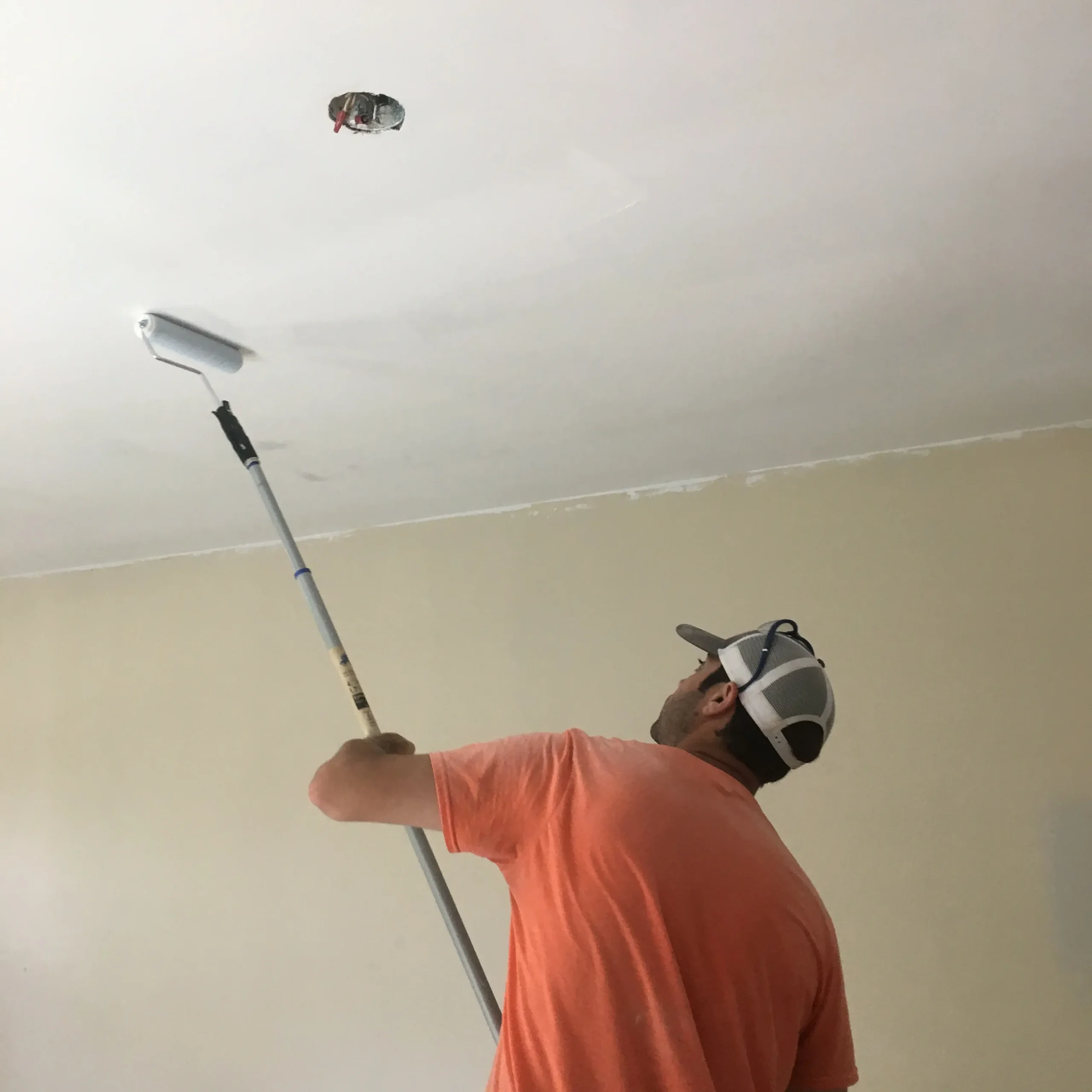 Contractor painting white ceiling with roller on extension pole indoors