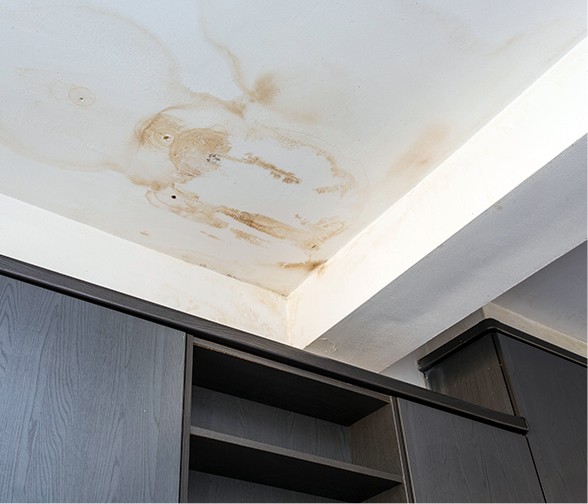 Brown water stains on white ceiling above dark wood cabinets from ice dam leak