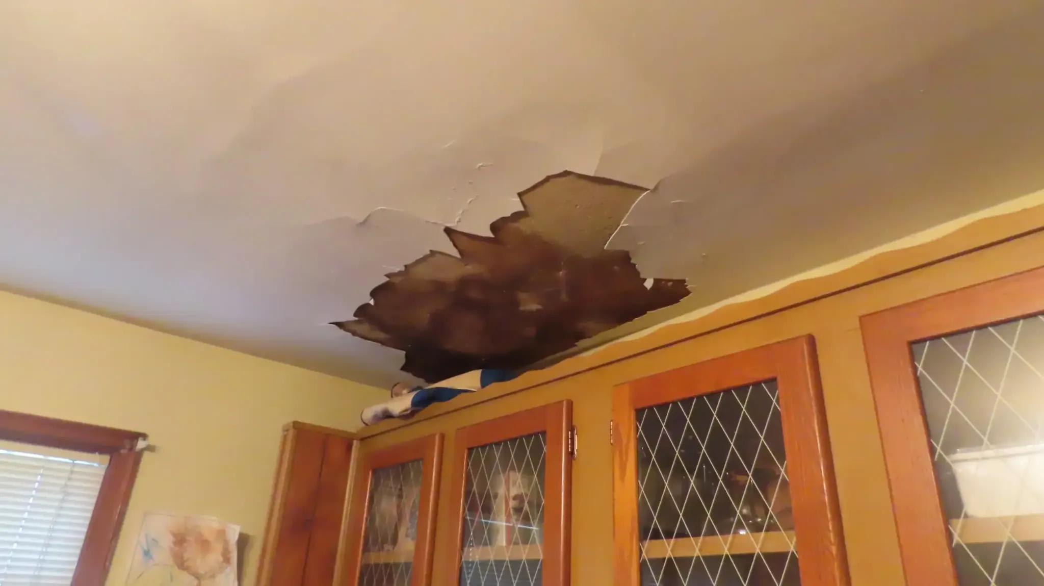 collapsed ceiling with water damage and dark staining above wooden cabinets