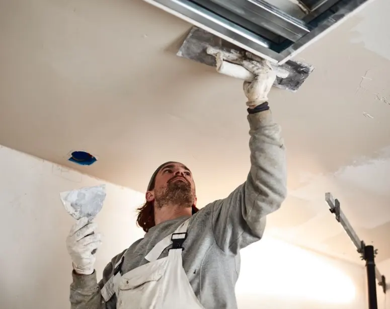 Worker plastering and patching drywall ceiling after ice dam water damage repair