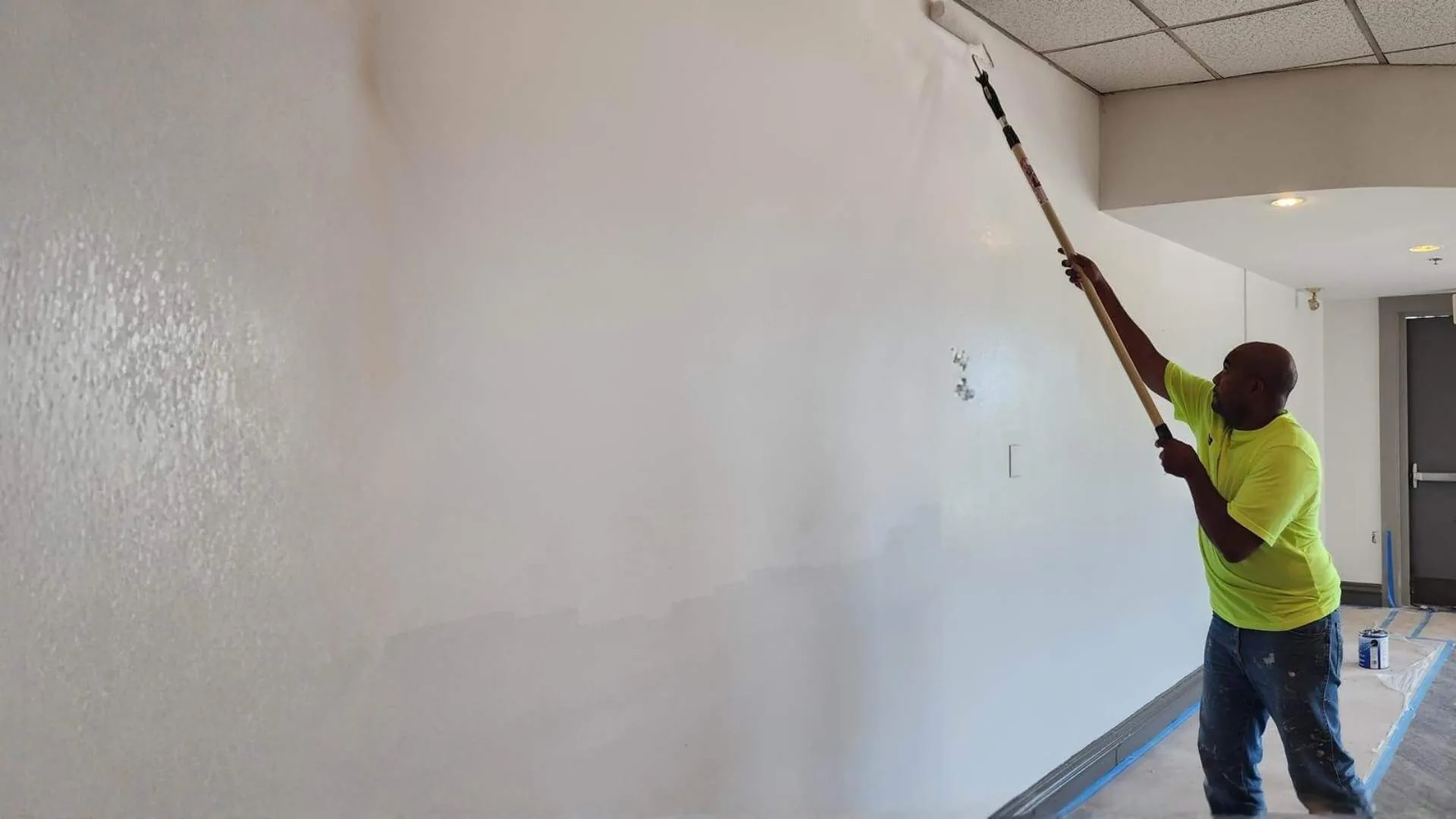painter rolling white paint on interior wall with extension roller