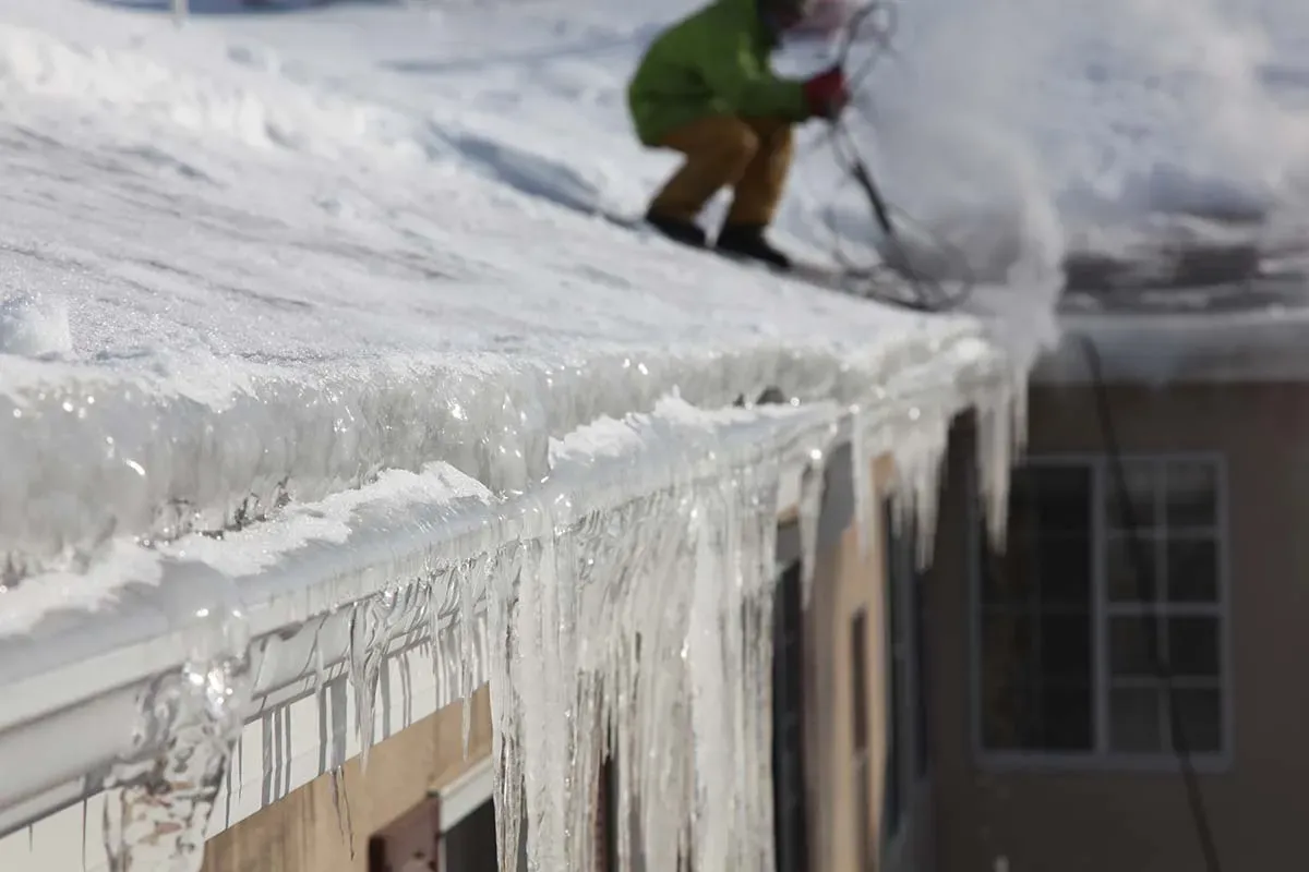 Worker removing ice dam from snow-covered roof with steaming tool